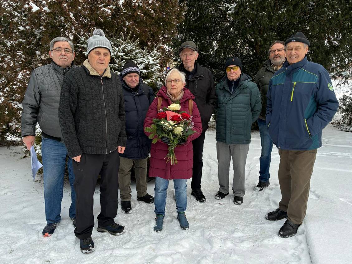 Das Foto zeigt eine Gruppe von Menschen, eine Person hält einen Blumenstrauß.