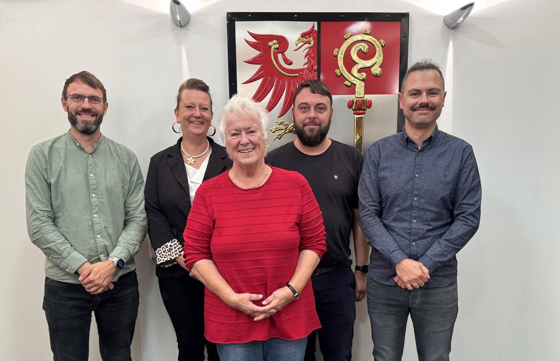 Das Foto zeigt fünf Personen vor dem Wappen des Landkreises im Foyer des Kreistagssitzungssaales.