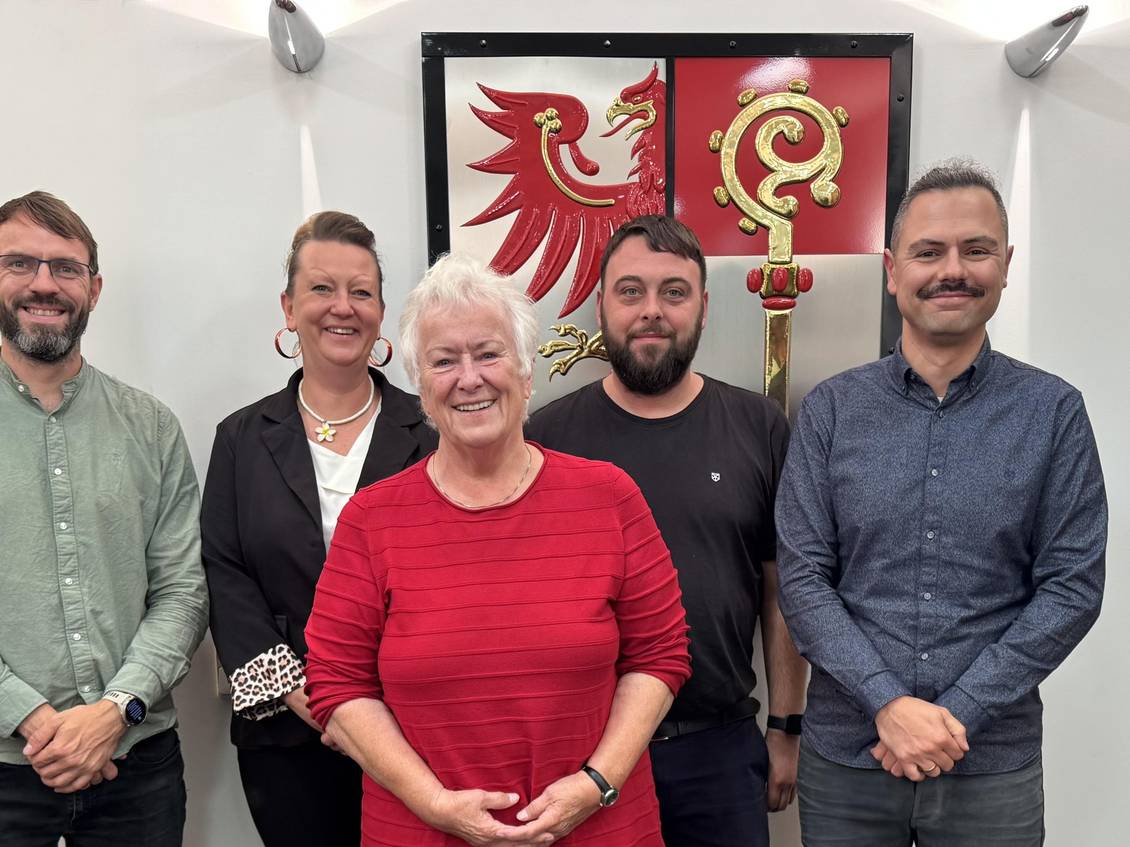 Das Foto zeigt fünf Personen vor dem Wappen des Landkreises im Foyer des Kreistagssitzungssaales.