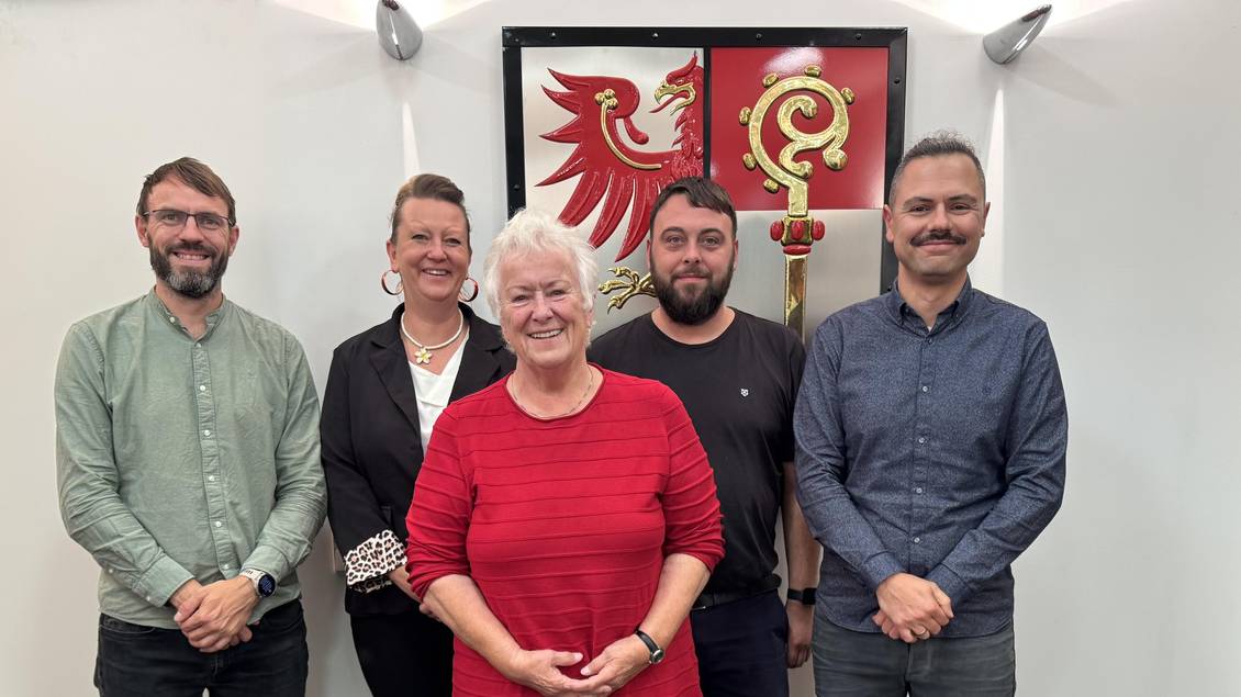 Das Foto zeigt fünf Personen vor dem Wappen des Landkreises im Foyer des Kreistagssitzungssaales.