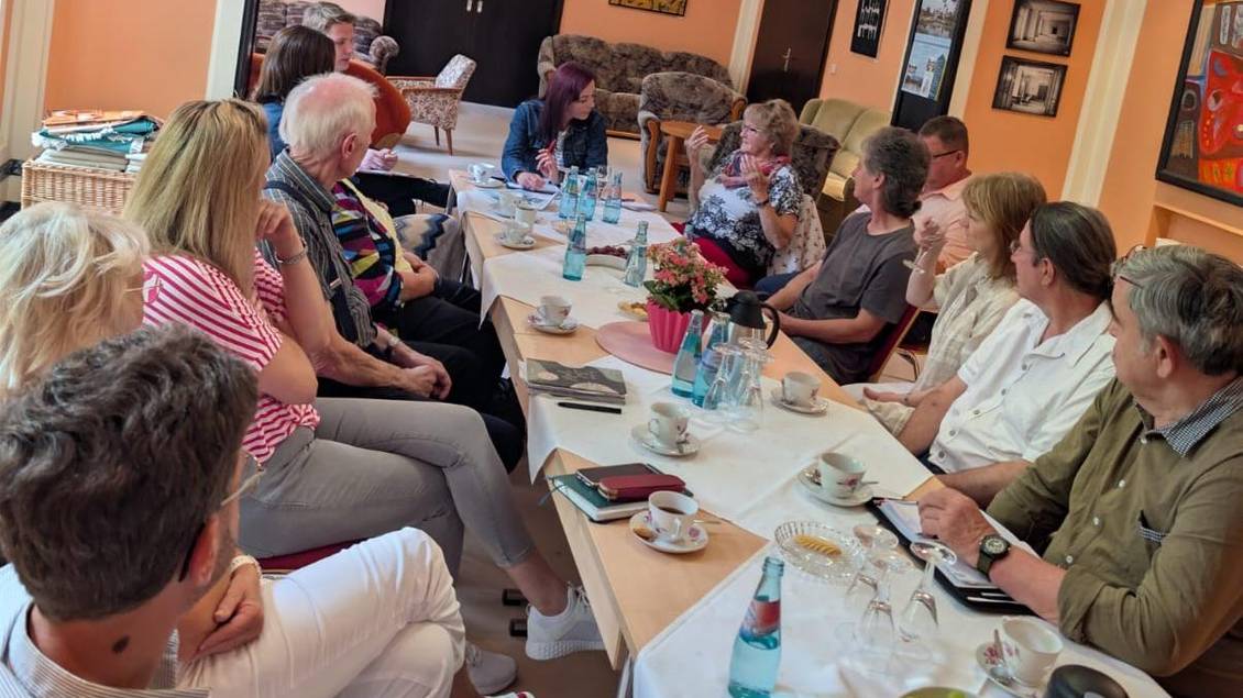 Das Foto zeigt mehrere Personen an einem langen Tisch während eines Gespräches.