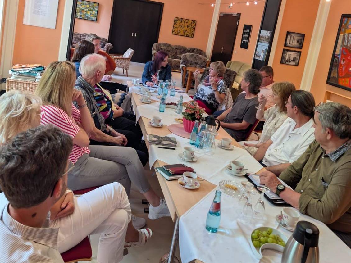 Das Foto zeigt mehrere Personen an einem langen Tisch während eines Gespräches.